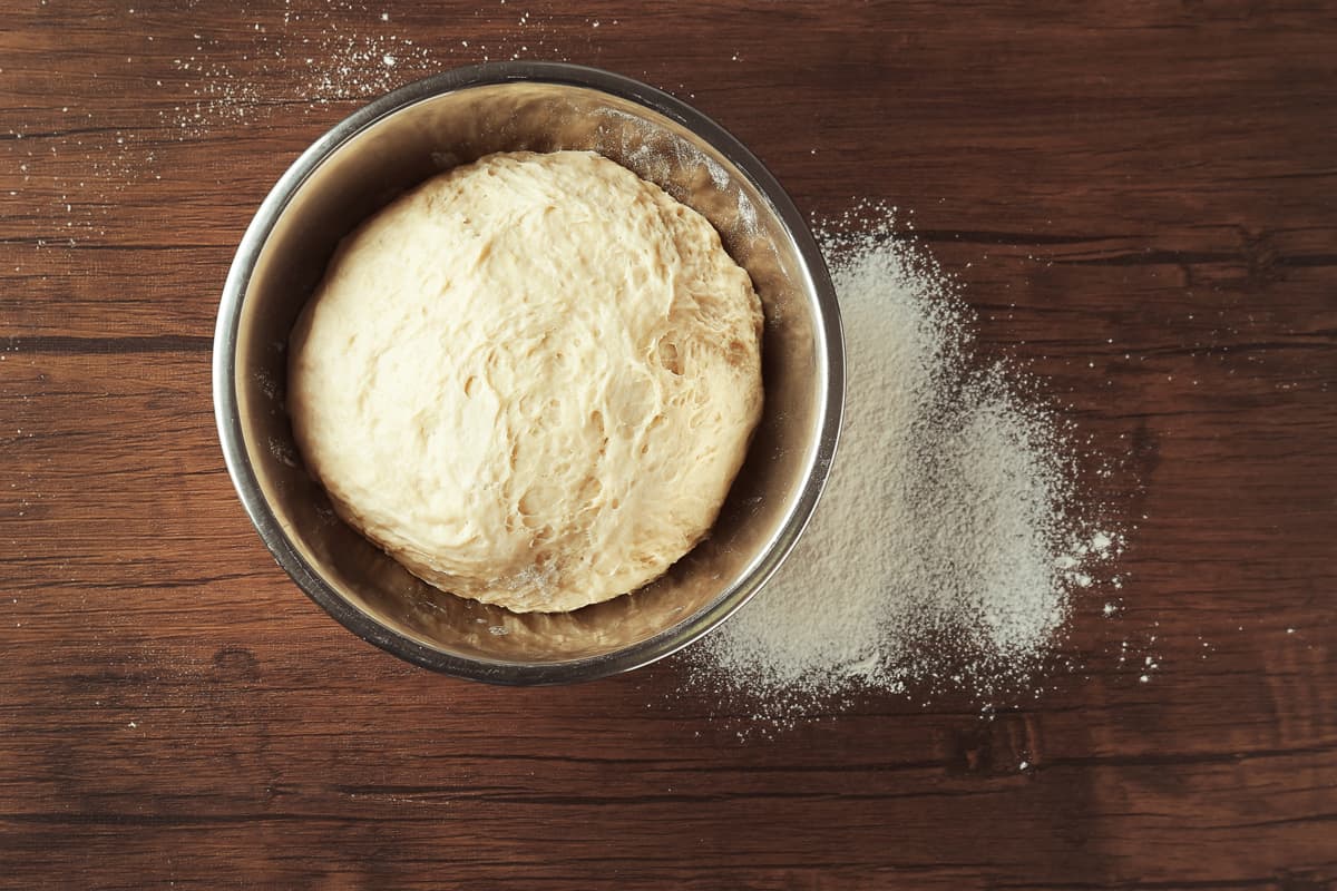 面包生面团混合在一个不锈钢碗面粉传播一个木制的桌子上