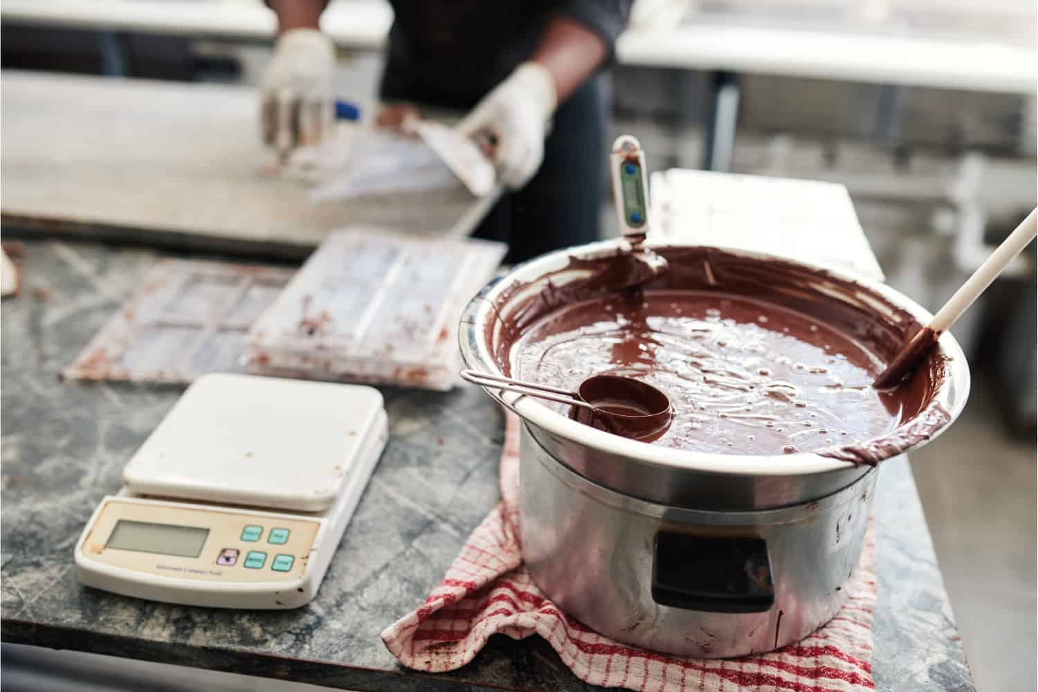 在手工巧克力制造工厂的桌子上，贝恩玛丽的融化巧克力正在混合和温度监测
