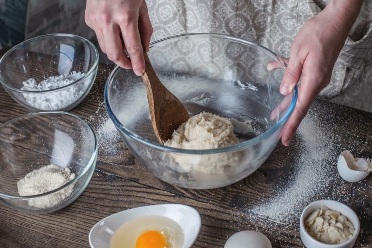 女人用铲子搅拌面团。鸡蛋,糖,杏仁放在桌上,附近什么大小的碗里做面包吗?