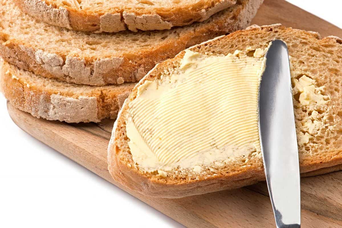 一把刀传播奶油涂到面包上”width=