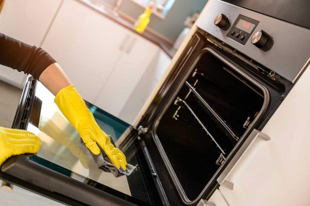 近距离观察戴着黄色橡胶手套的女人用抹布清洁烤箱的手