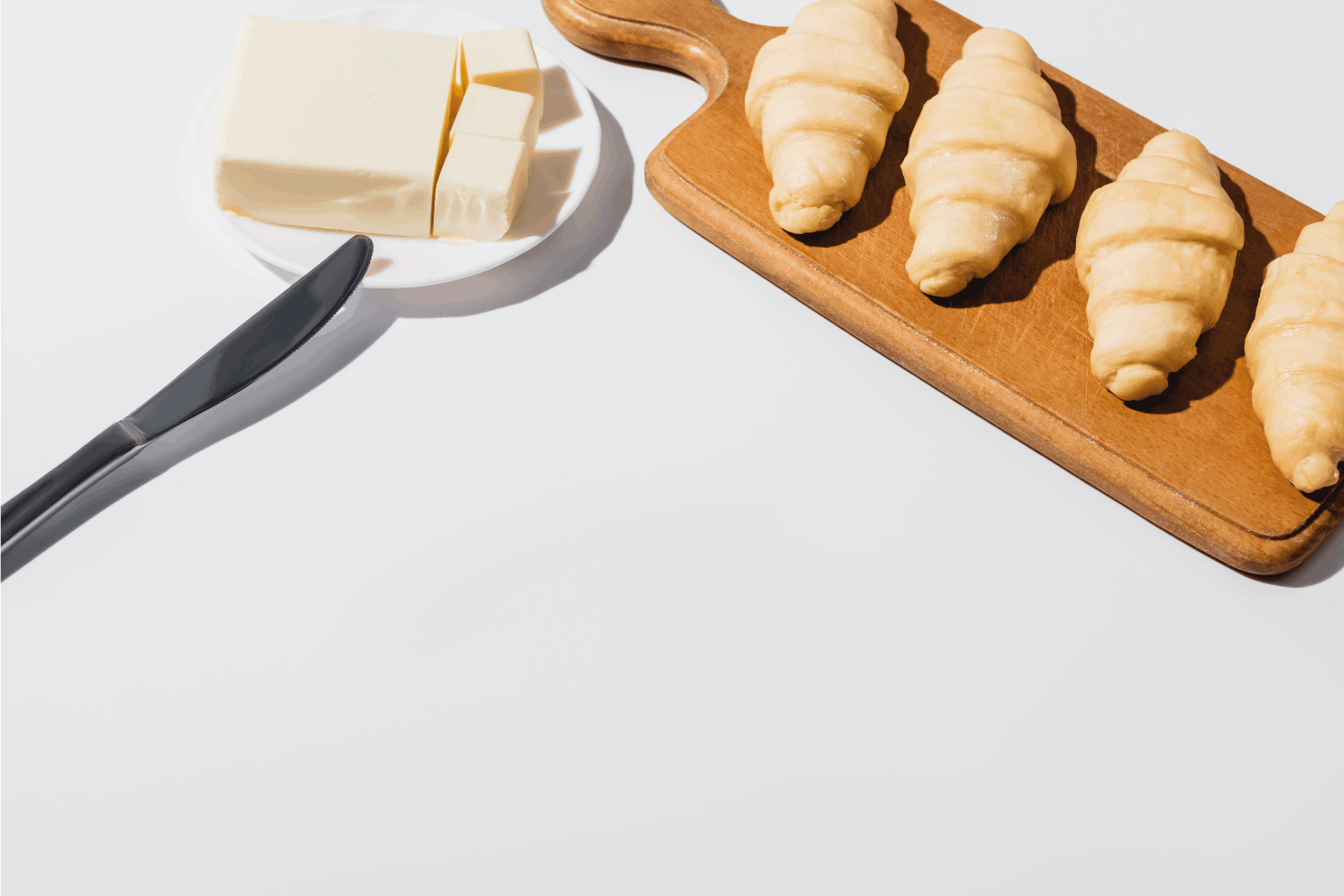 新鲜的生牛角包放在木砧板上，靠近黄油，用刀放在盘子上