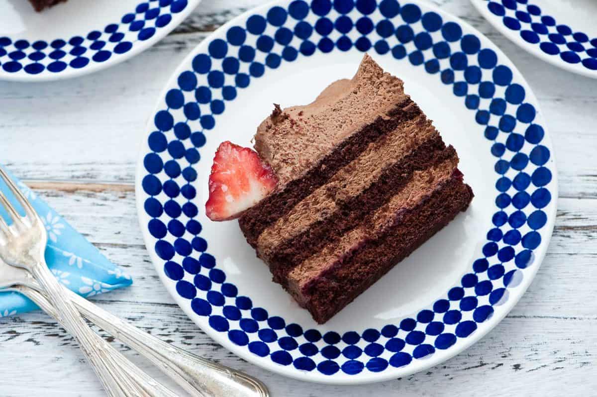白色木质背景的盘子里有一片浆果水果巧克力蛋糕＂width=