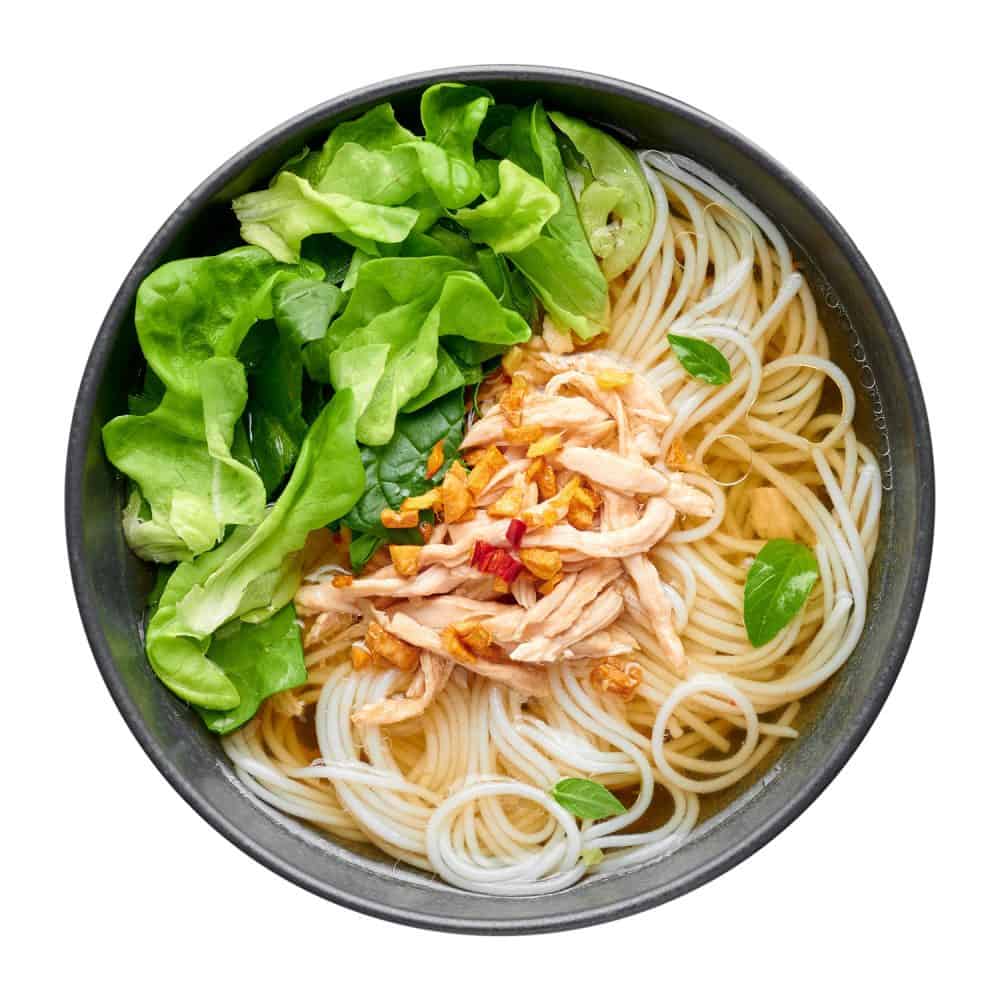 泰式鸡汤盛在碗里，旁边有绿叶蔬菜和脆蒜