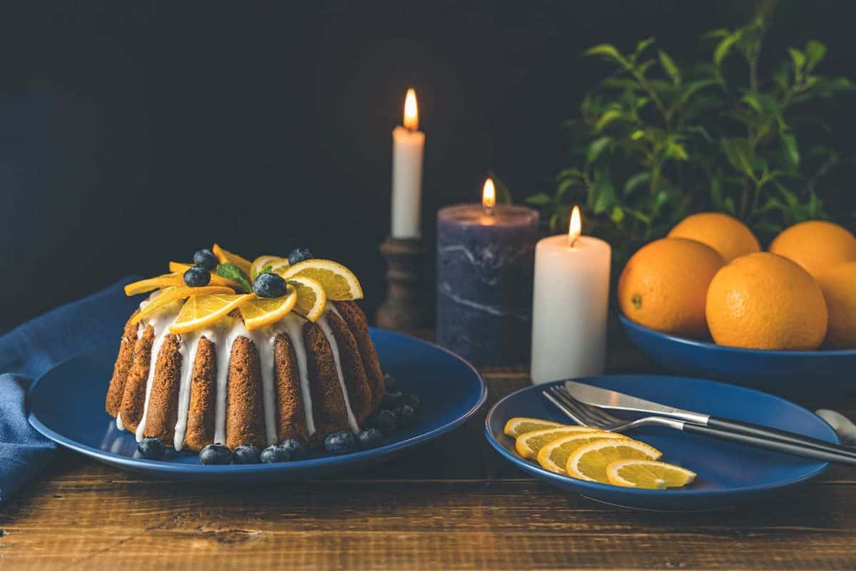 橘色蛋糕，蓝莓环绕的水果，蜡烛，植物和餐具在深色的木制背景
