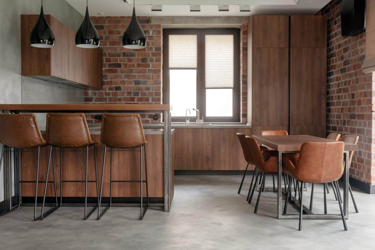 现代的室内设计，明亮宽敞的餐厅，包括棕色木制家具，柜台上的吧台凳和柔软舒适的椅子，桌子上有水泥效果的阁楼风格