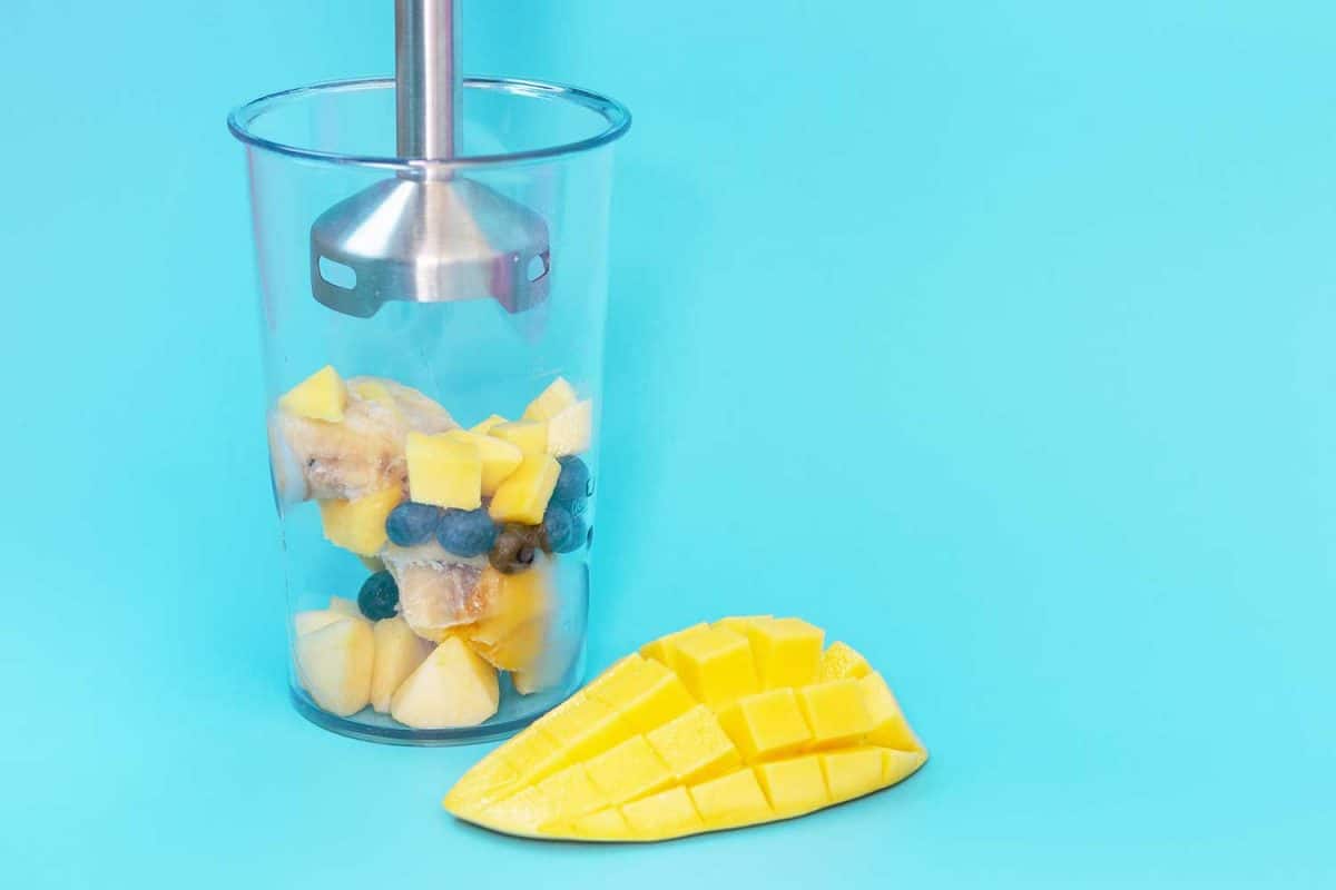 塑料碗，水果和浸入式搅拌机在蓝色背景特写