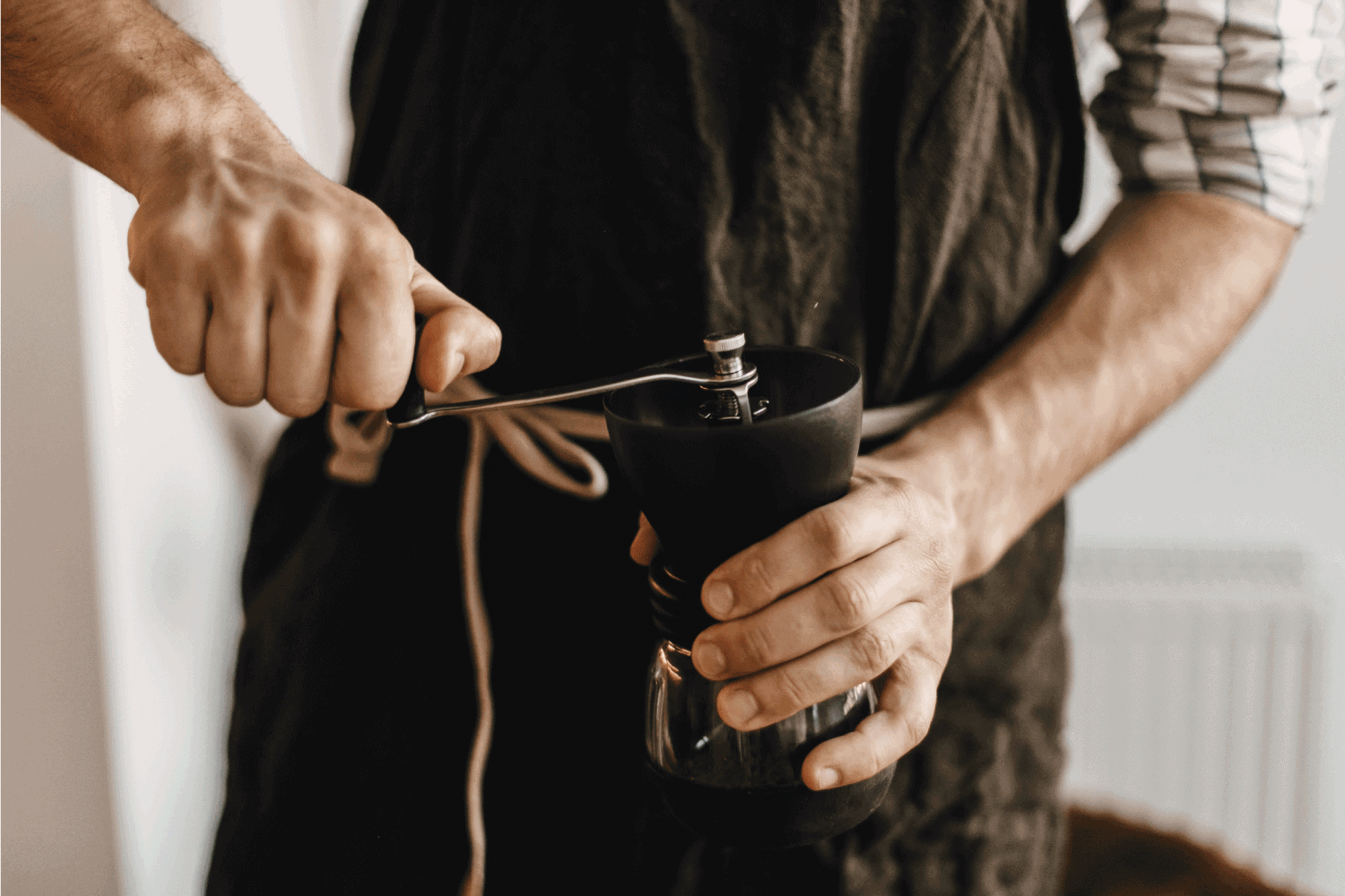专业的咖啡师在黑色时尚围裙磨咖啡气压机，替代冲泡方法。手握手工磨咖啡豆机