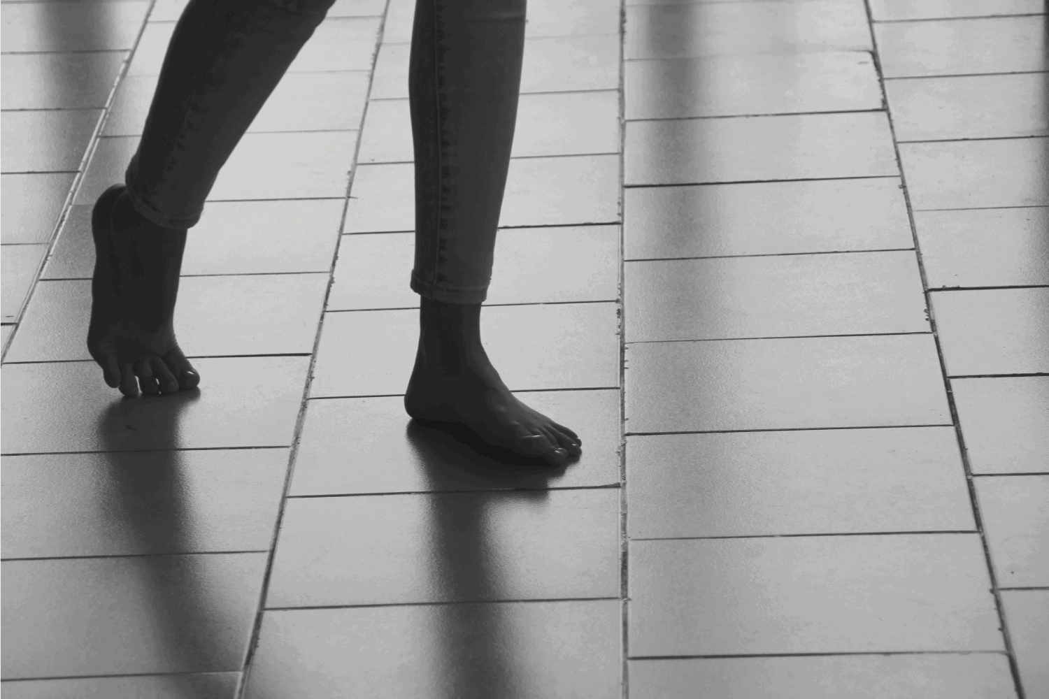 抽象的女性双脚走在瓷砖地板上投下阴影。这个女孩正赤脚走在瓷砖地上