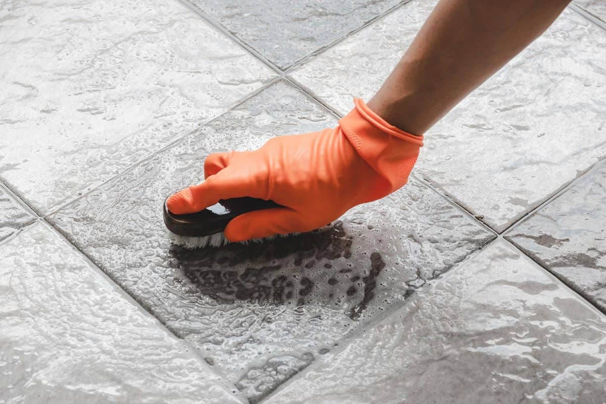 戴着橙色橡胶手套的人的手被用来转换对瓷砖地板的擦洗清洁