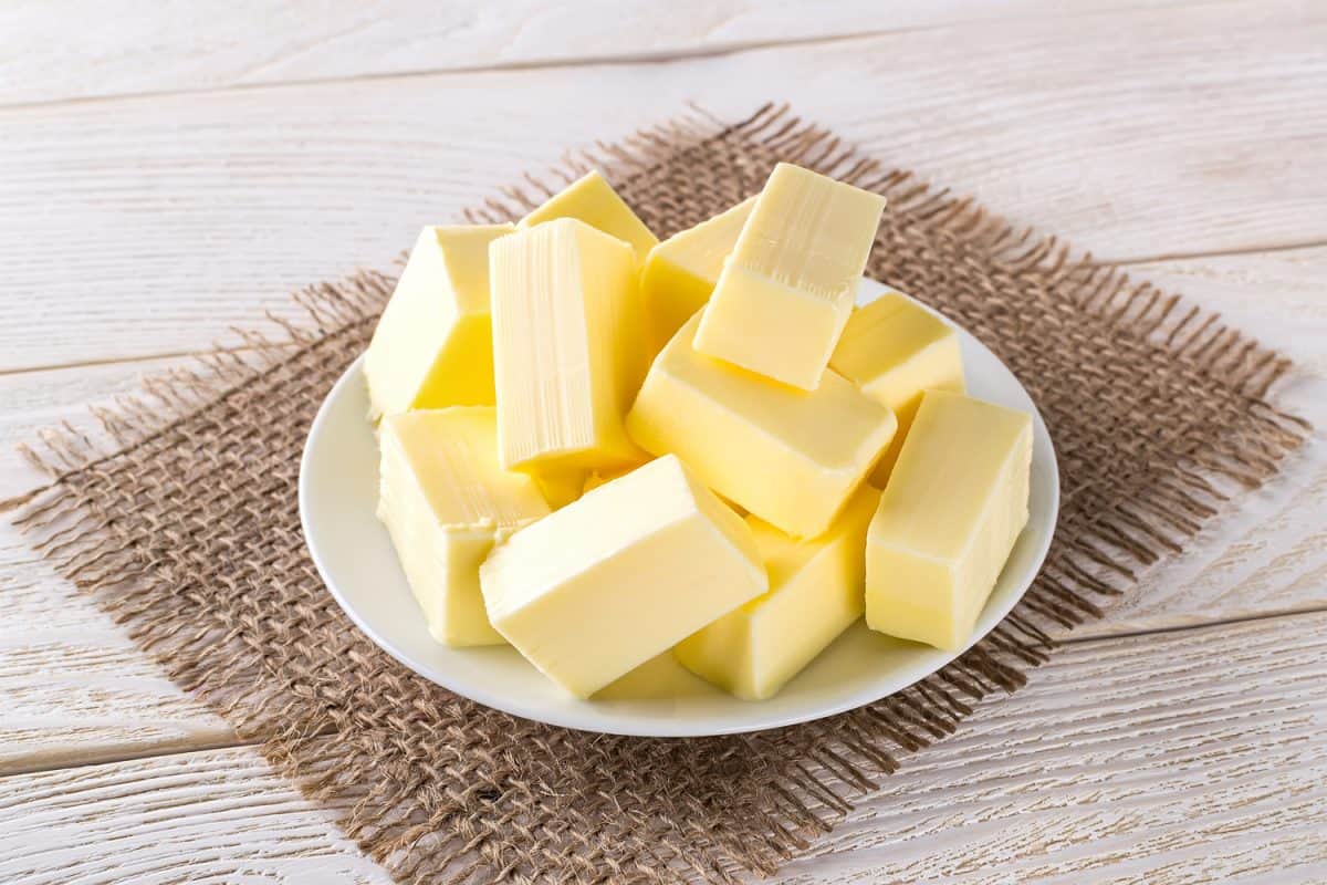 白色木桌上方的白色碟子上放着长方形的新鲜黄色黄油。奶制品。三明治黄油。天然脂肪营养素。前视图。