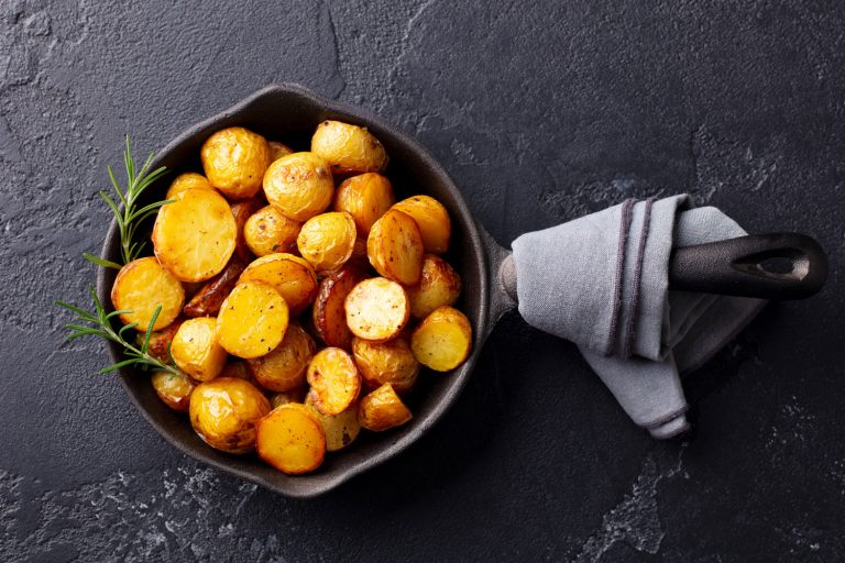 用铁锅烤小土豆。深灰色背景，烤土豆前应该先煮吗?