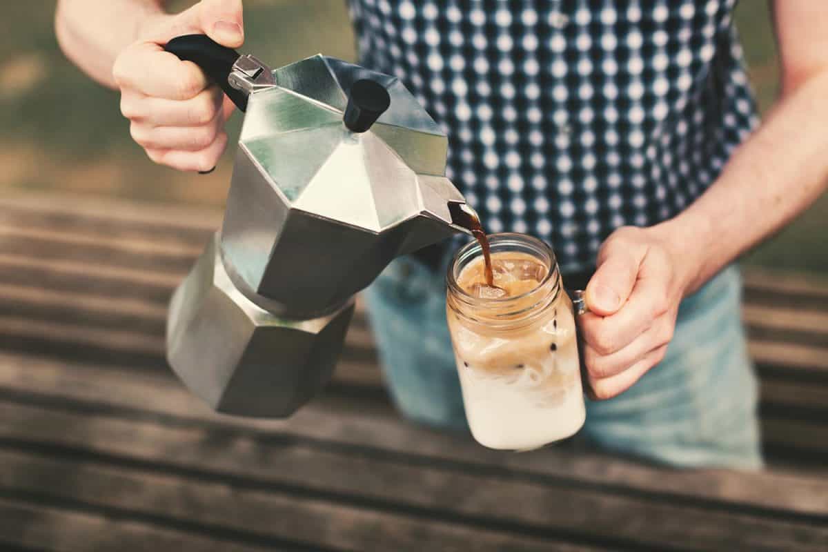 一个男人从咖啡机里倒咖啡到一个装有牛奶和冰的罐子里