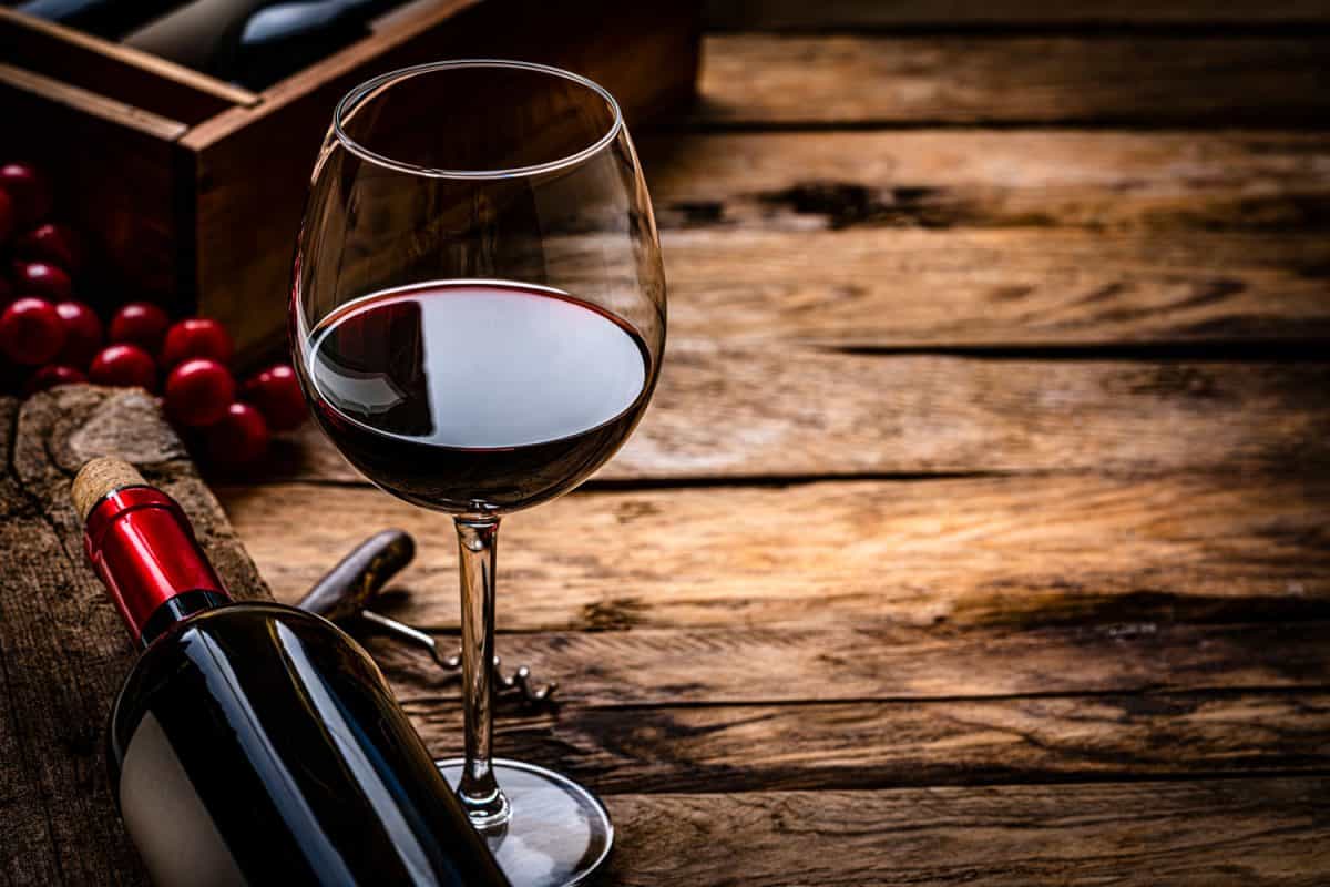 一瓶红酒旁边放着红酒和红葡萄的薄酒杯