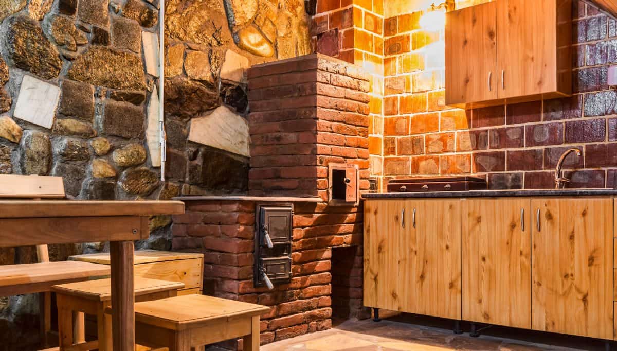 一个极具乡村风格的厨房，墙上有装饰性的石头，一个小砖烤箱，bd手机下载木制橱柜和桌子