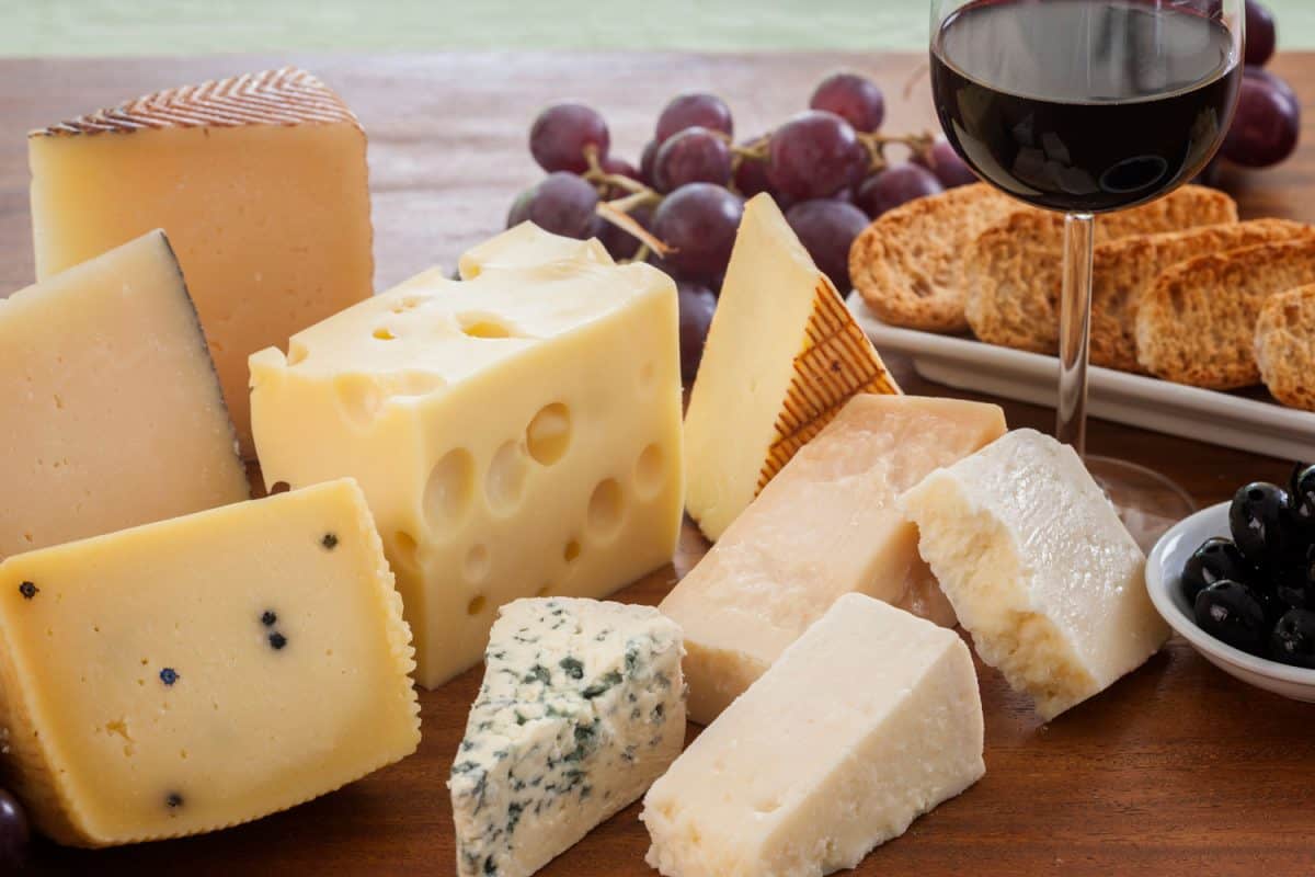各式各样的奶酪(如薄荷、蓝奶酪、佩克里诺干酪、帕尔玛干酪和曼彻戈干酪等)与面包、葡萄、黑橄榄和一杯红酒一起放在木桌上。奶酪应该在室温下食用吗?
