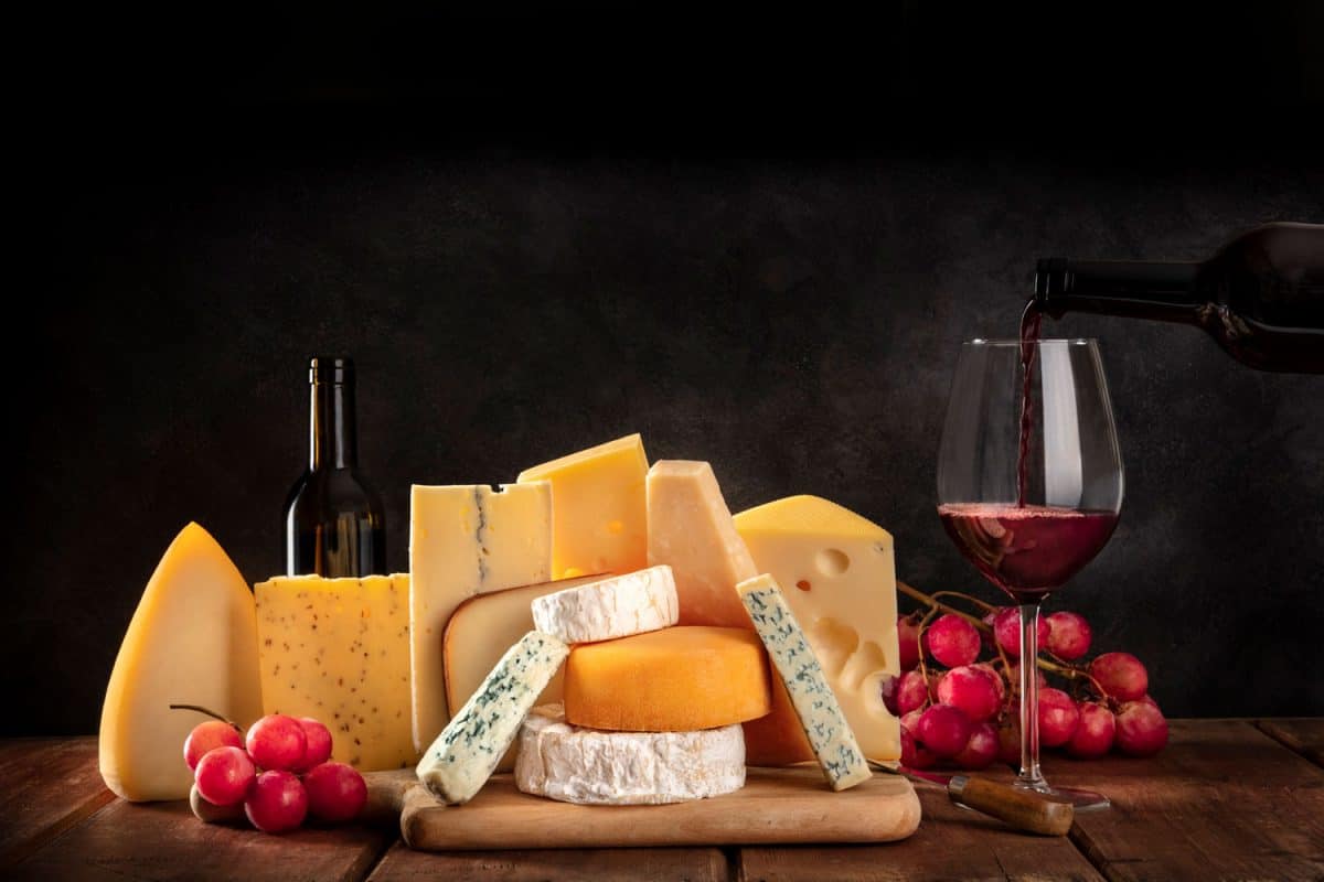 奶酪与葡萄和倒酒，侧视图在一个黑暗的背景与复制空间，你应该用箔纸或保鲜膜包裹奶酪?