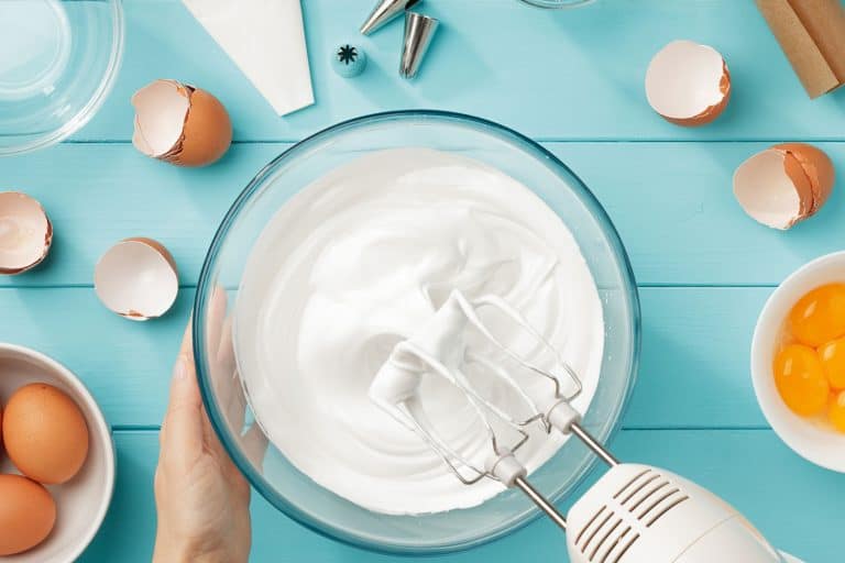 蛋清制作奶油完美的山峰在玻璃碗混合器和手放在蓝色的木桌上。一步一步的酥皮饼干顶视图,一夜之间如何存储酥皮