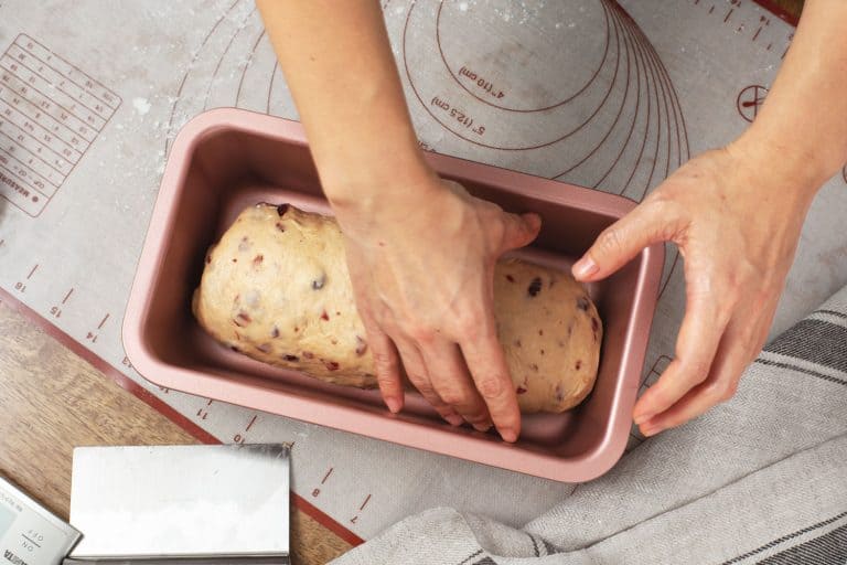 女人的手准备蔓越莓面包面团在粉红色的面包盘,16个类型和大小的面包锅
