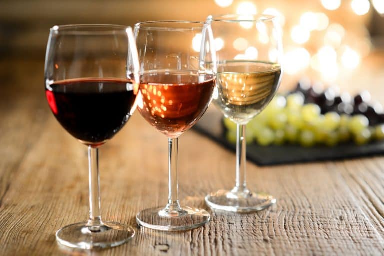 在以葡萄为背景的木制餐桌上，在昏暗的灯光下，三杯白、红、玫瑰葡萄酒。