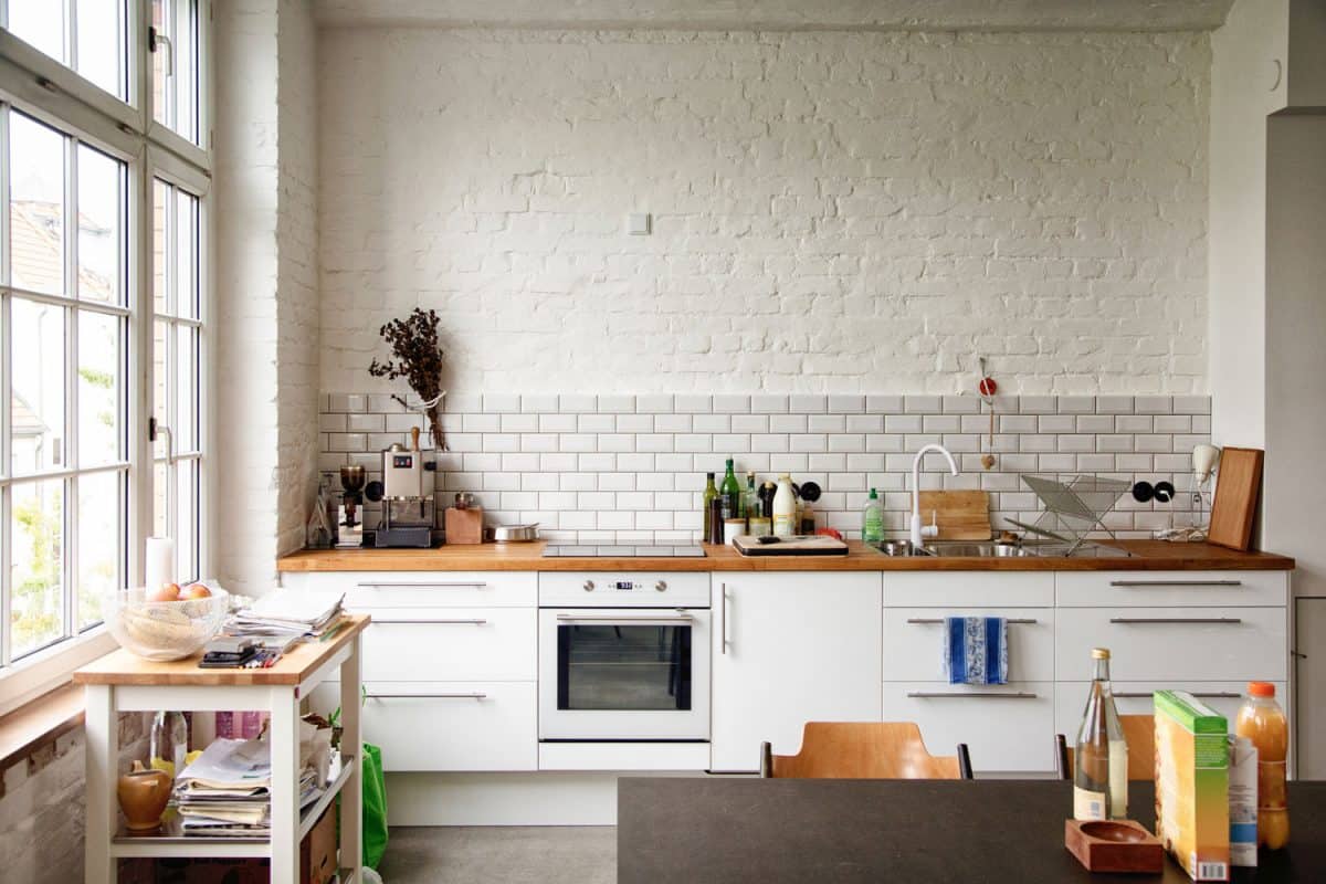 一个华丽的现代厨房，有白色的橱柜，木bd手机下载制的台面，侧面有一扇巨大的白色框窗