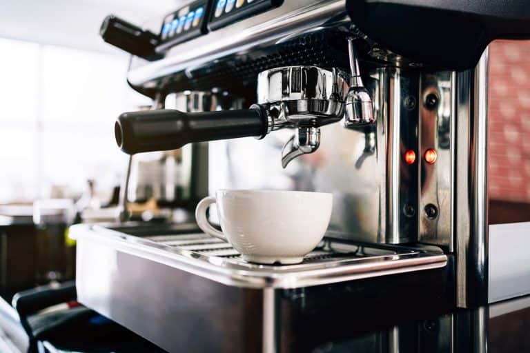 咖啡师特写手插入金属过滤的咖啡机,等待倒热在杯黑咖啡,你多久反冲咖啡机吗?