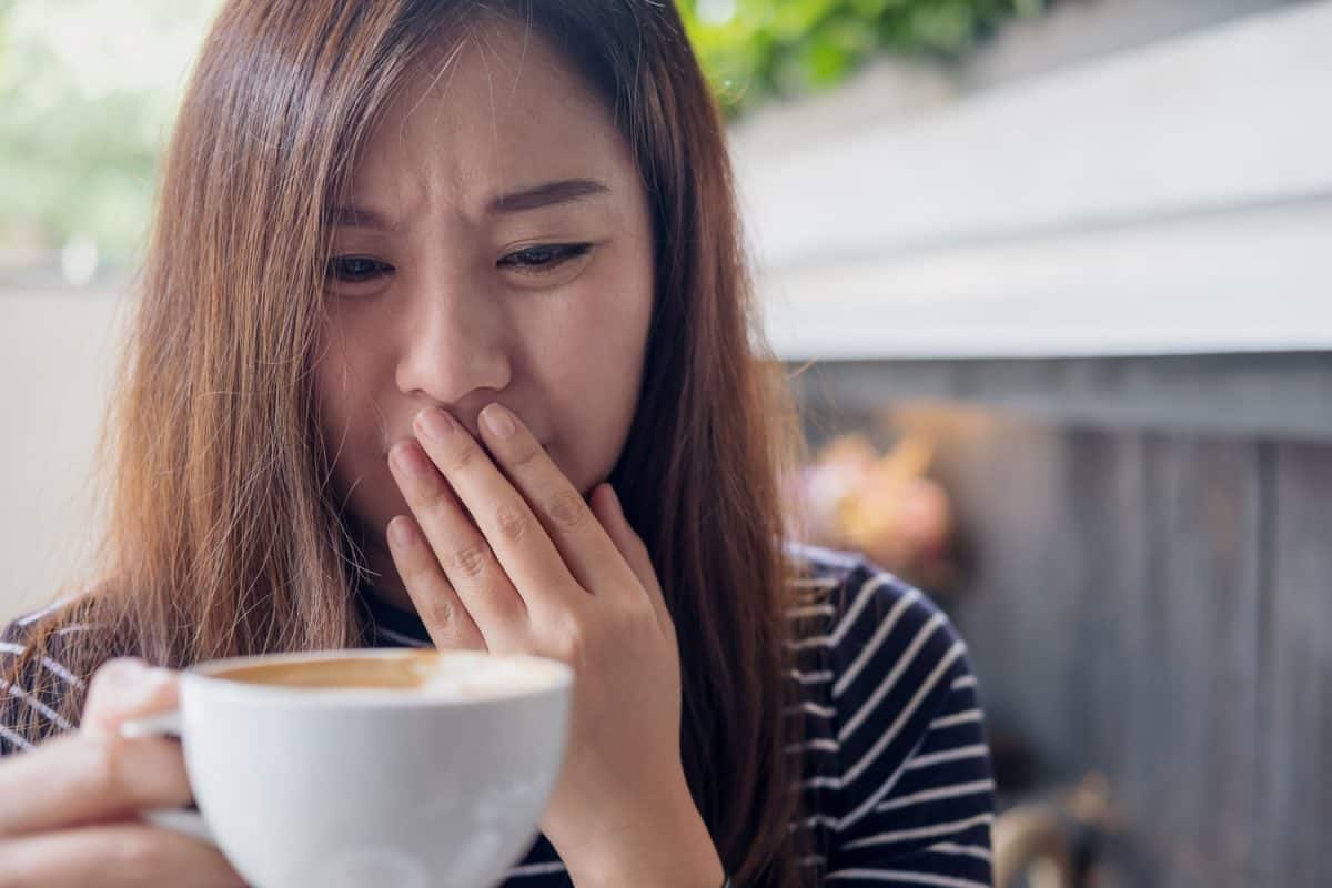 特写图像的亚洲妇女拿着热咖啡，感觉奇怪和气味不好的咖啡店