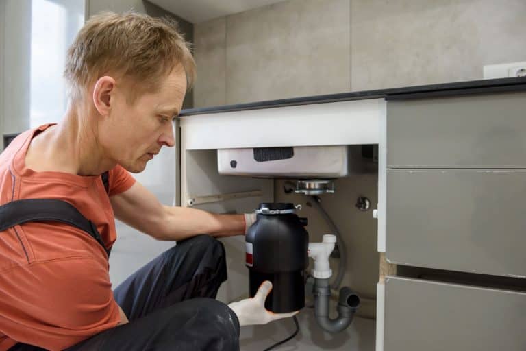 工人正在为厨房水槽安装家用垃圾碎纸机，1/2马力Vs 3/4马力垃圾处理器:选择哪一个bd手机下载