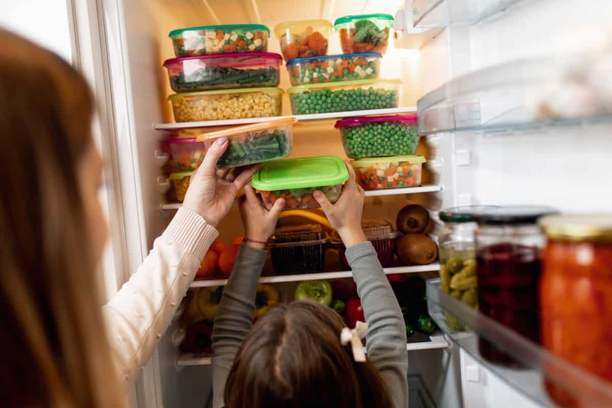 一名妇女和她的孩子把装满蔬菜和其他水果的特百惠放入冰箱
