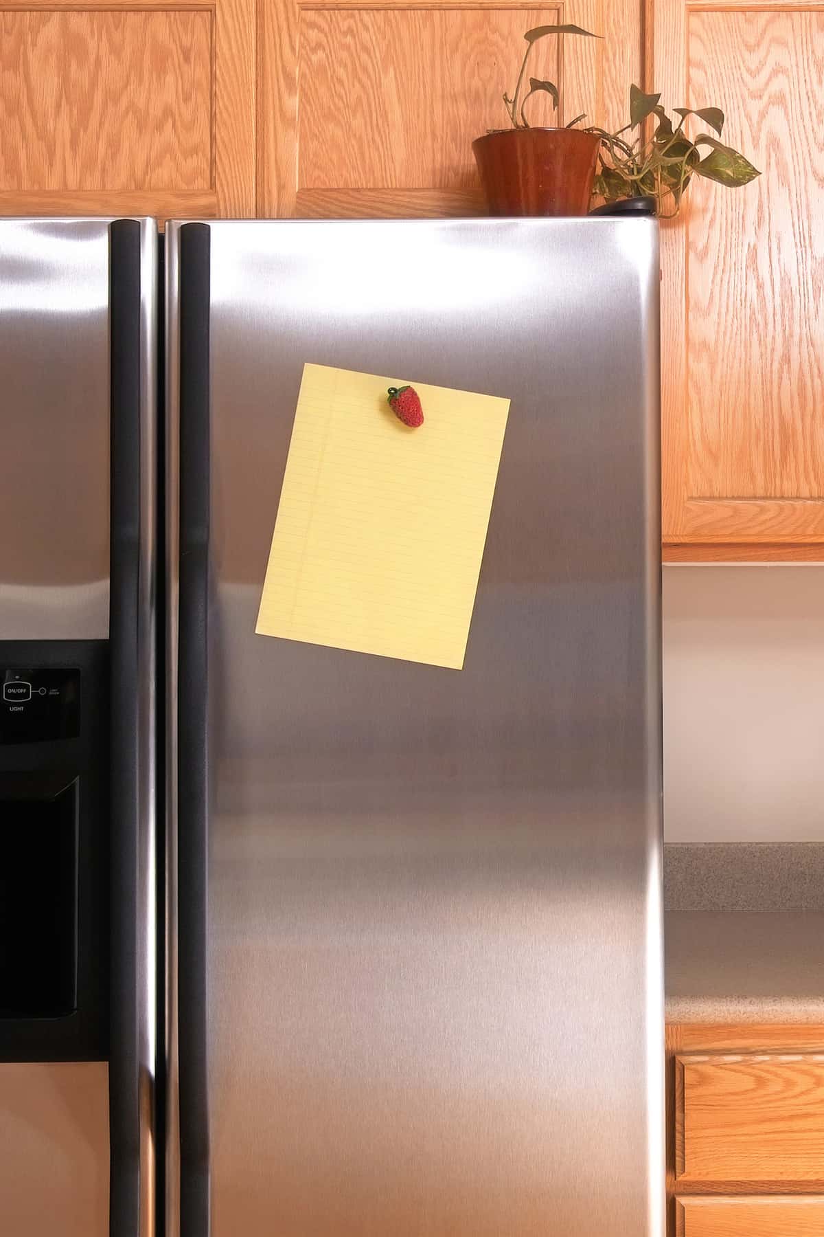 一张空白的黄色便条纸，用草莓磁铁固定在冰箱门上。