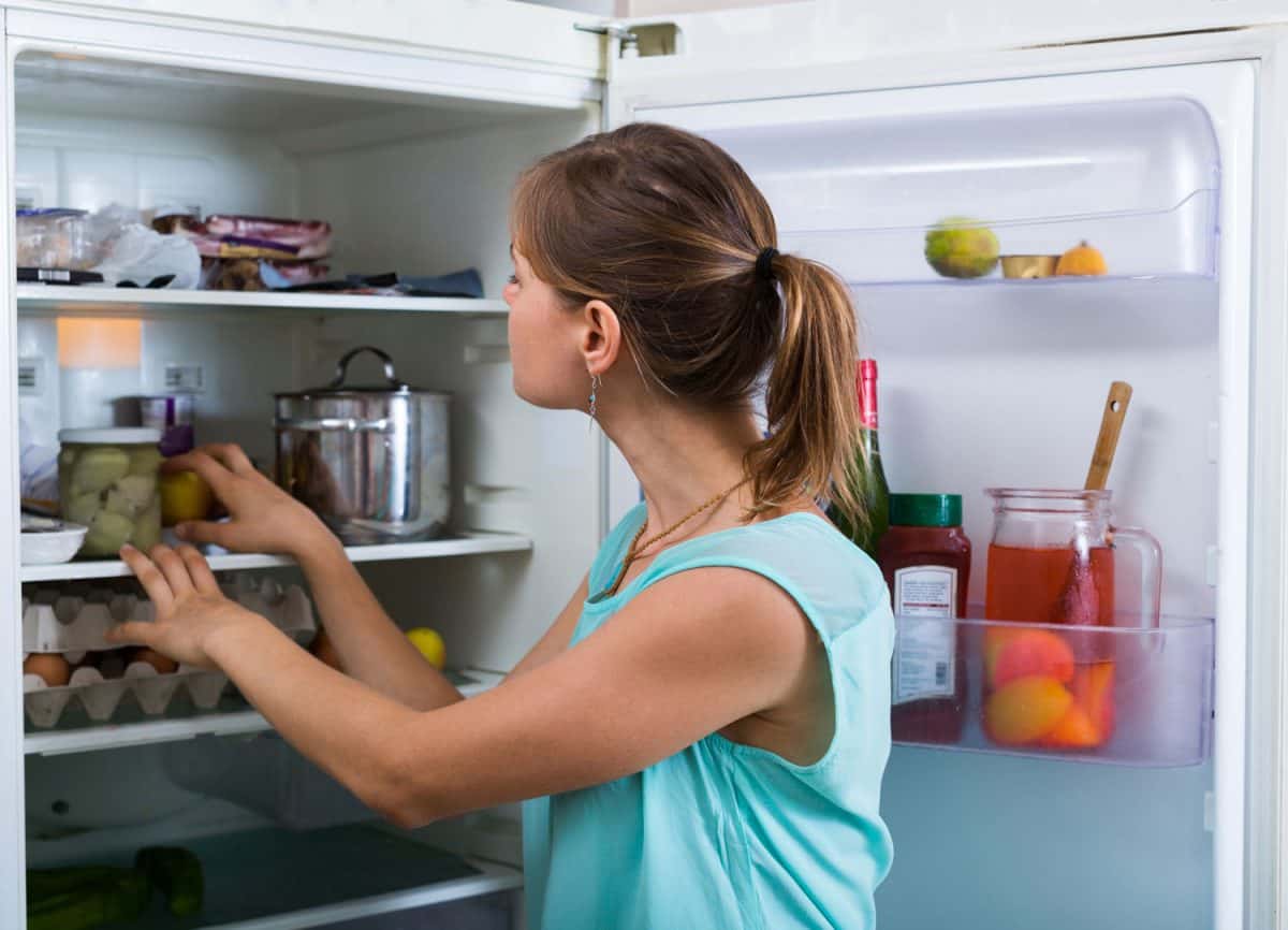 年轻女子站在冰箱旁，里面装满了产品