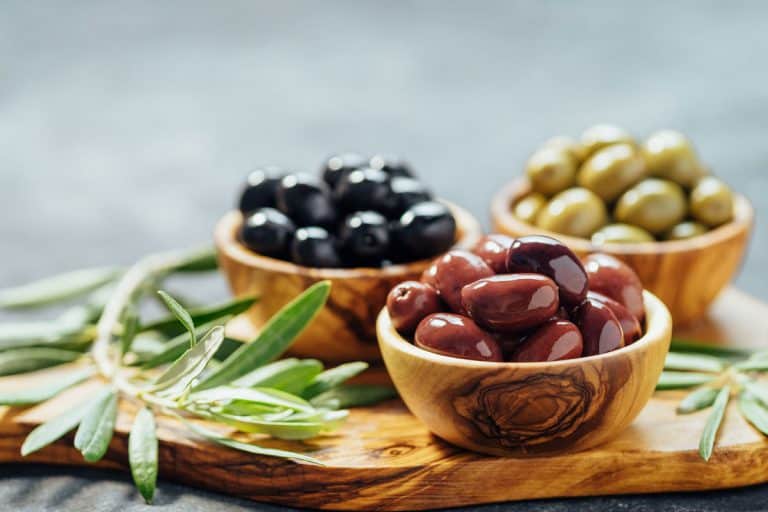 不同类型的橄榄木制碗橄榄和橄榄油在木砧板和新鲜的橄榄叶,橄榄去年冰箱里多久?