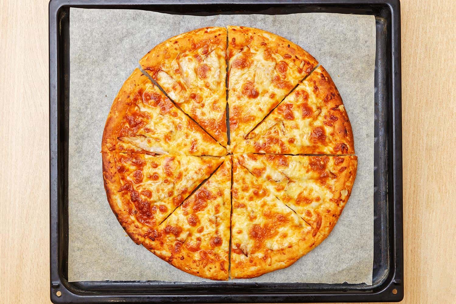 新鲜的鸡肉奶酪披萨放在烤盘和羊皮纸上＂width=