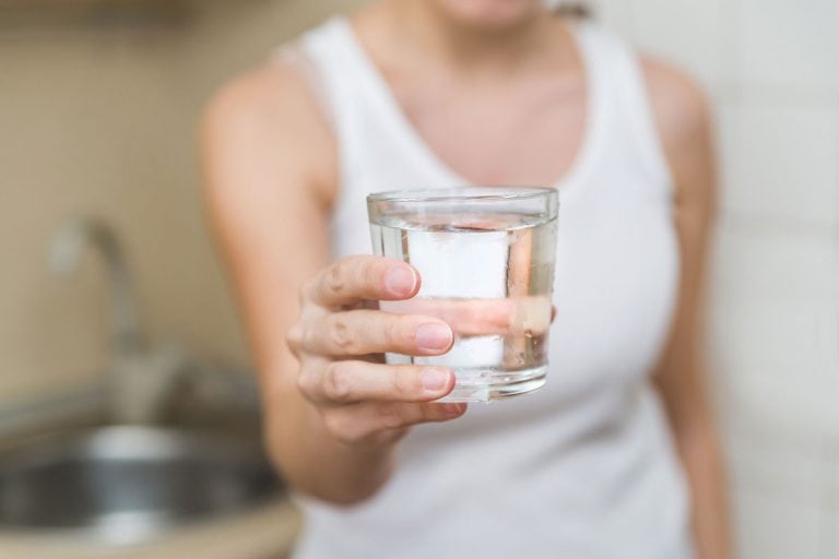 一个健康的年轻女子握着一杯水。在透明玻璃清洁的饮用水在你手中特写,喝杯有多重?