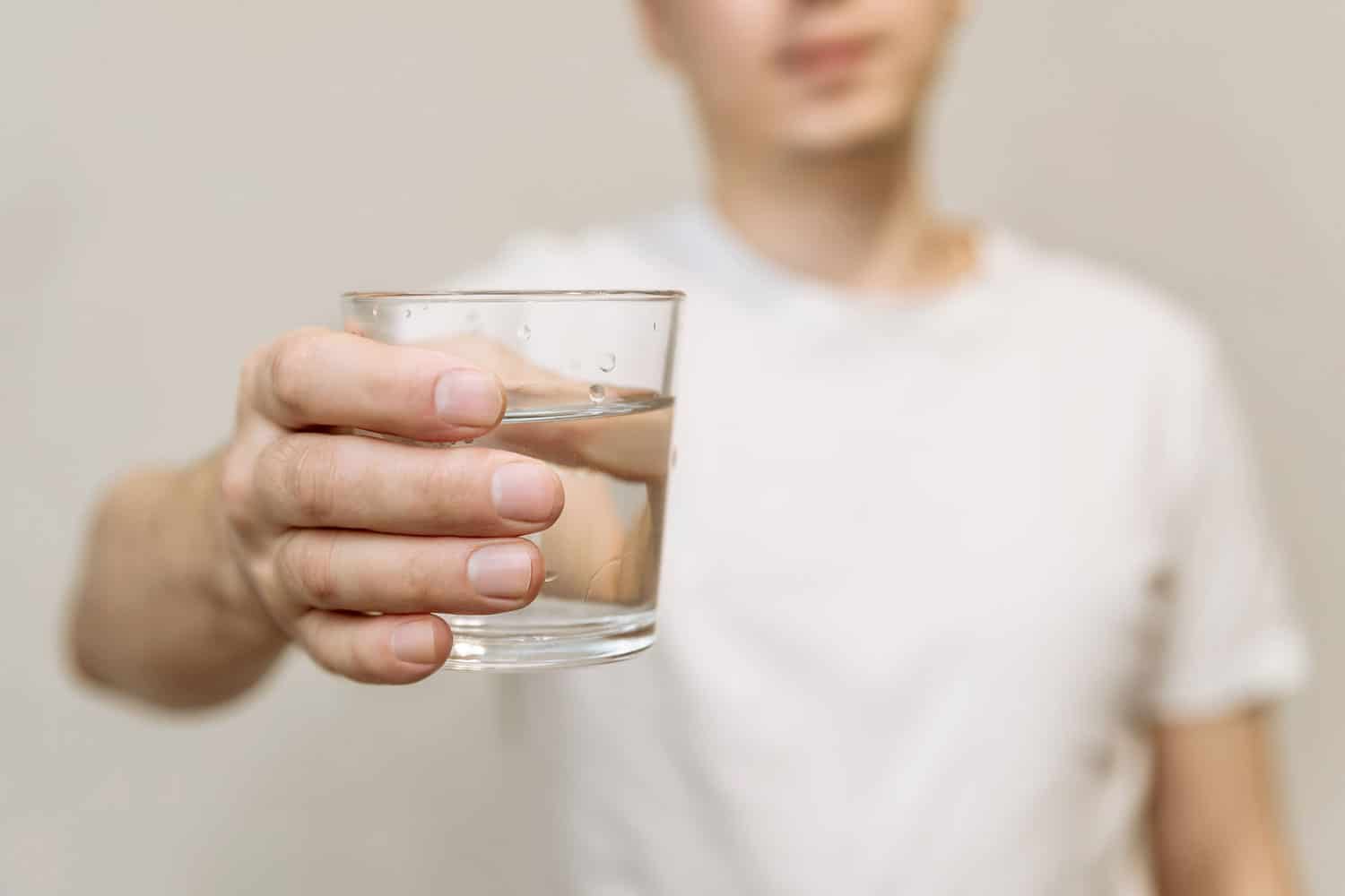 一个穿着白色t恤的年轻人端着一杯清澈的饮用水