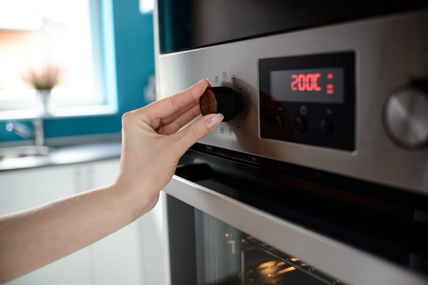 近距离的女人的手设置温度控制烤箱。显示器显示设定的温度为200摄氏度