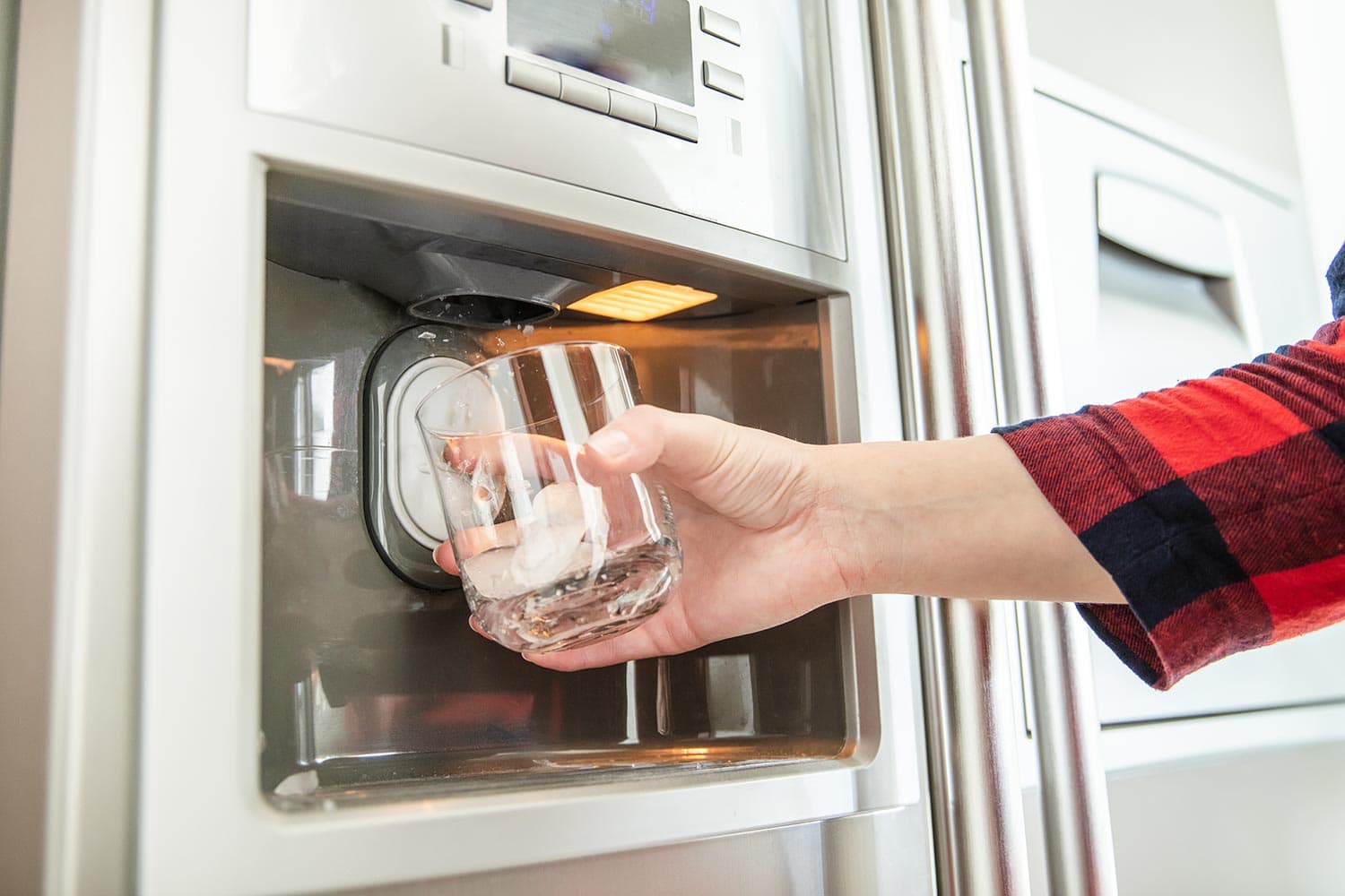 女人的手拿着玻璃杯，用冰箱制作新鲜干净的冰块