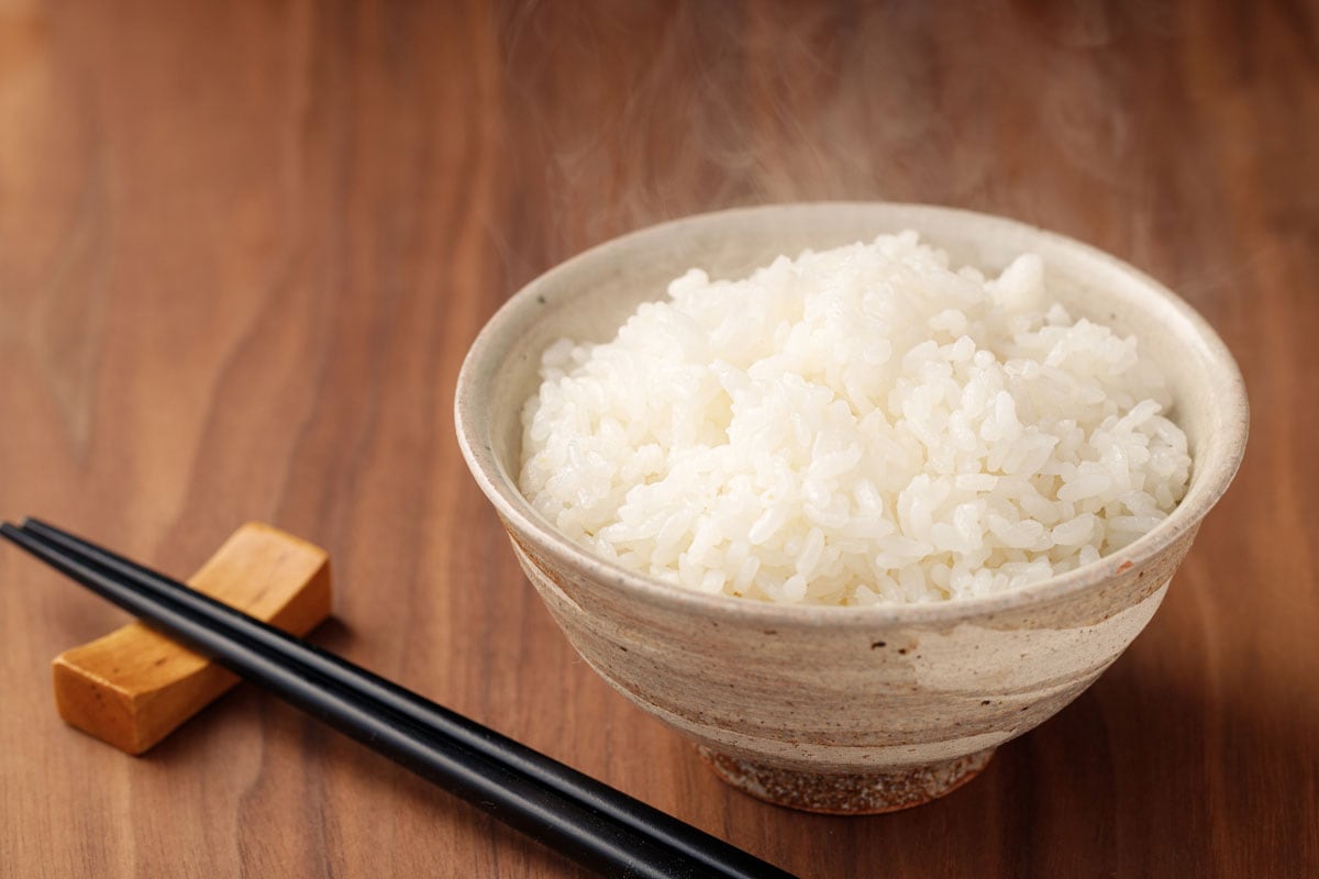 白碗盛着热气腾腾的米饭，木桌上摆着黑色的筷子
