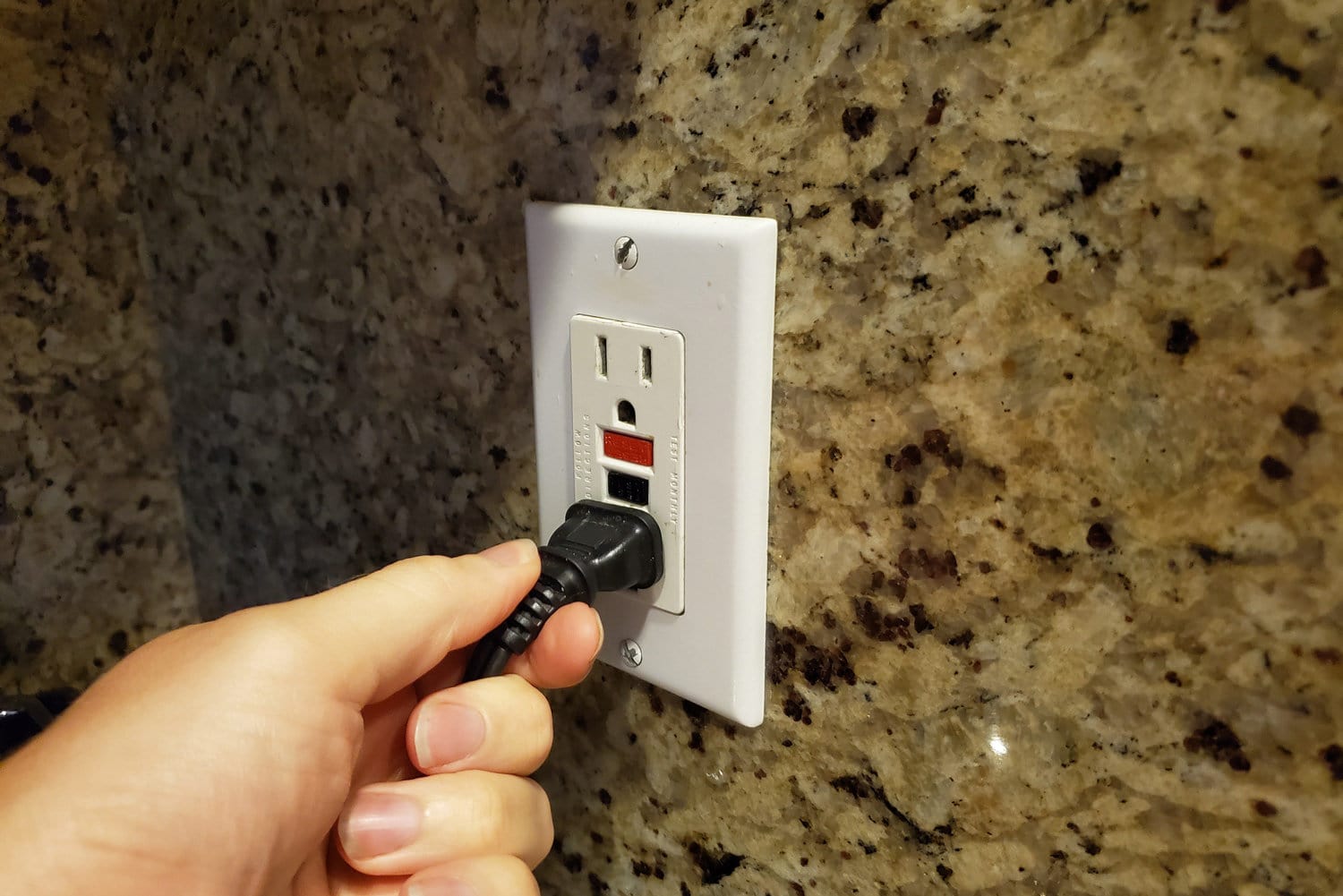 特写，个人视角的人手图像，一个男人将电源线插入家庭房间墙上的接地故障电路中断器(GFCI)电源插座