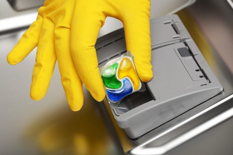 特写黄色橡胶手套的手把洗涤剂平板放在洗碗水——洗碗机豆荚和液体——选择为您的厨房bd手机下载