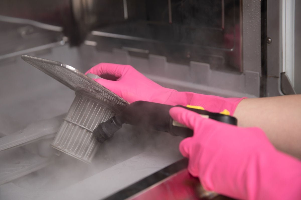 家庭主妇戴着橡胶手套，用热蒸汽清洗机清洗洗碗机过滤器