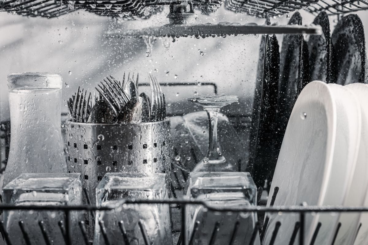 透明和黑白的盘子以及餐具和玻璃杯在洗碗机中清洗，内部视图，水滴和飞溅的水。