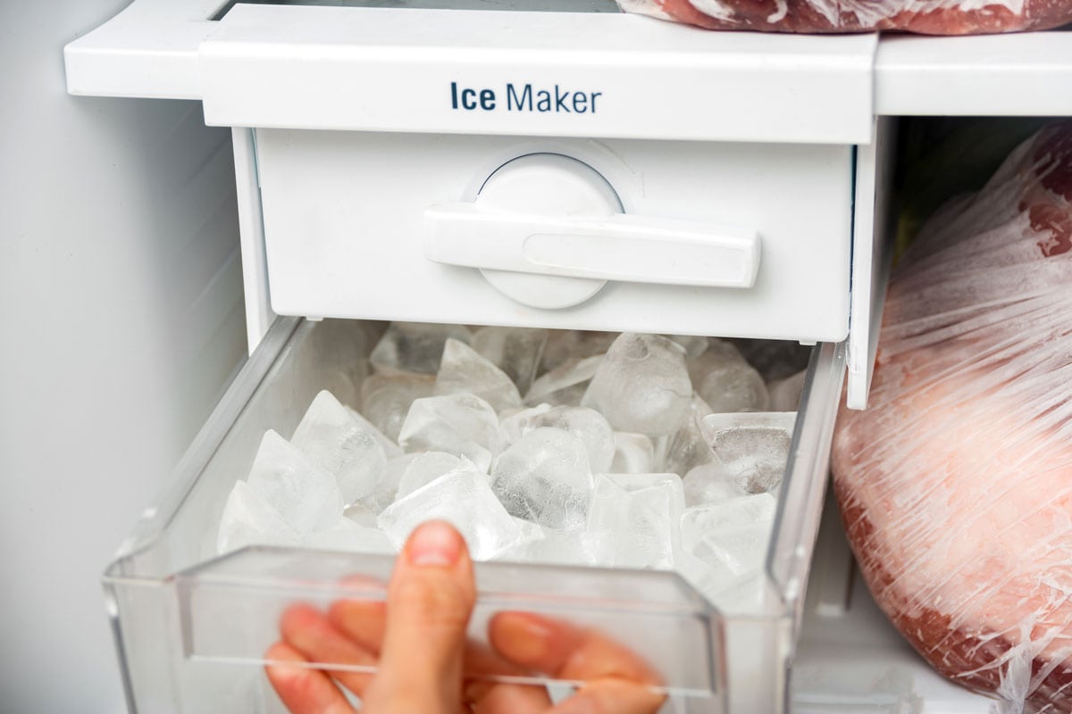 一名妇女打开冰箱里的制冰机托盘，取出冰块来冷却饮料