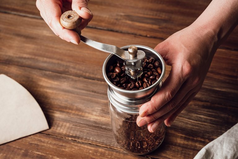 在手动咖啡研磨机研磨咖啡豆木桌上。你能在咖啡研磨机磨盐或食物处理器呢?