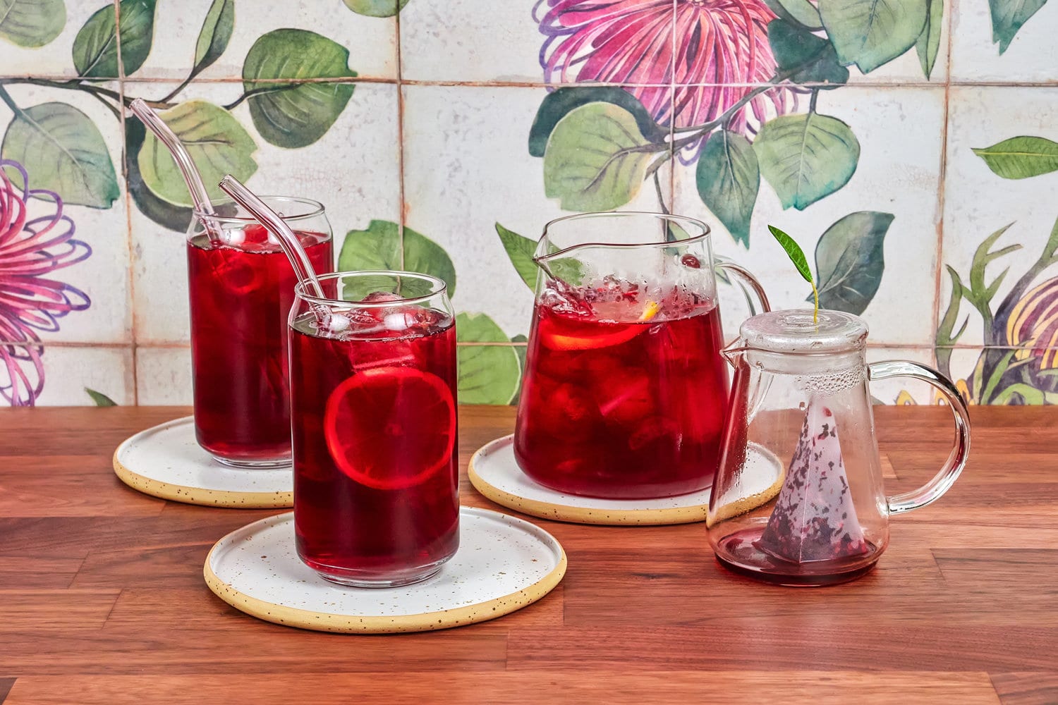 树莓冰茶在一个特殊的玻璃茶壶,两杯冰茶和硼硅酸盐吸管,在胡桃木桌子和瓷砖的背景。