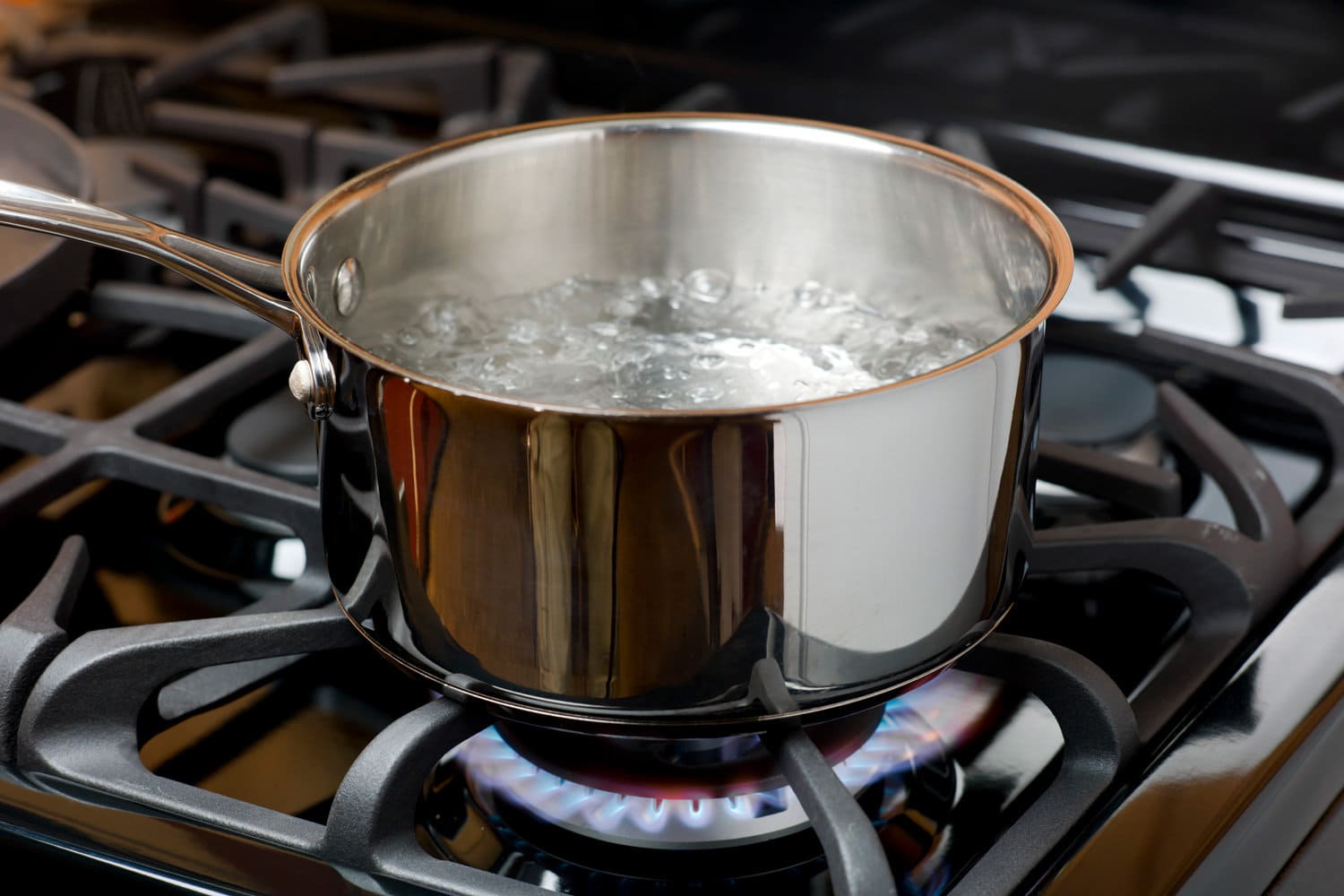 水在家庭厨房的煤气炉或炉灶上起泡沸腾。bd手机下载蓝色火焰和不锈钢锅。