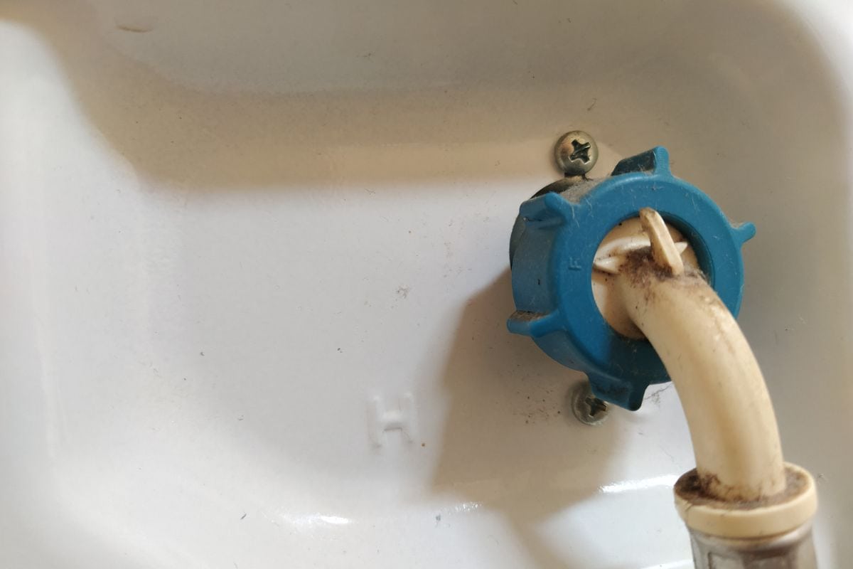 将洗衣机或洗碗机的软管连接到供水系统。一根管子用螺丝固定在家用电器的本体上。家庭作业和装修。蓝色螺栓连接软管和进水口。
