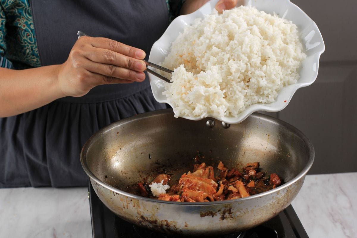 在平底锅中加入白米，炒泡菜，在厨房制作泡菜炒饭的烹饪过程bd手机下载