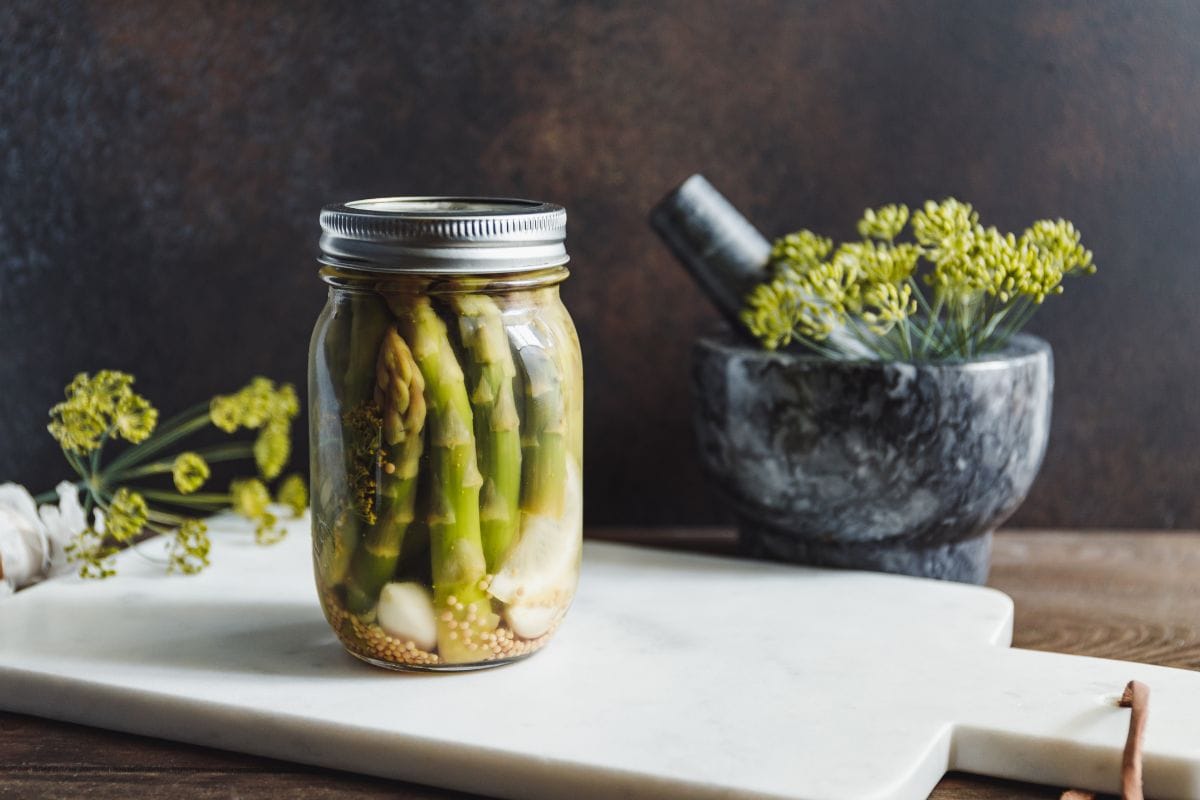 腌芦笋装在玻璃罐里，放在白色大理石托盘上。应季蔬菜罐头食谱。