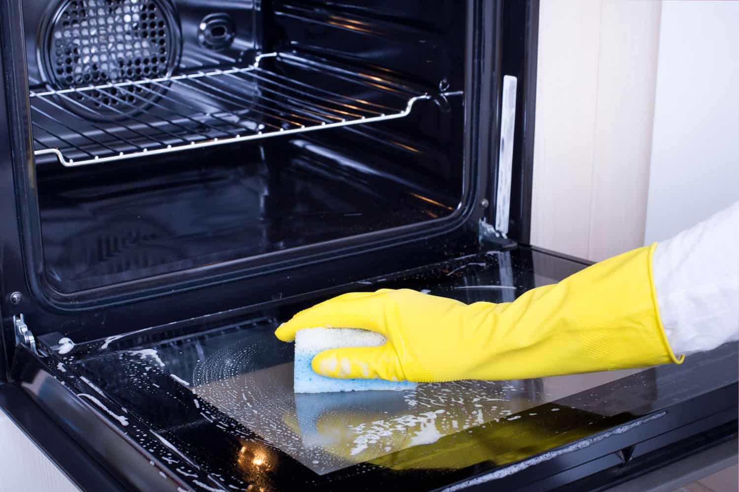 一位女士戴着手套，用海绵擦拭烤箱的玻璃门